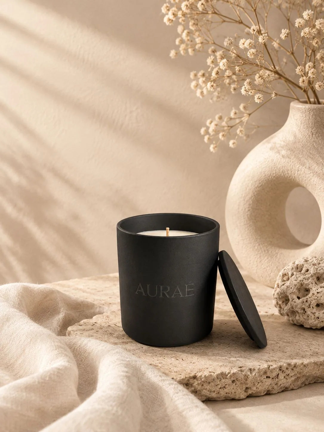 Auraé Midnight Silk black ceramic candle with lid, on travertine stone